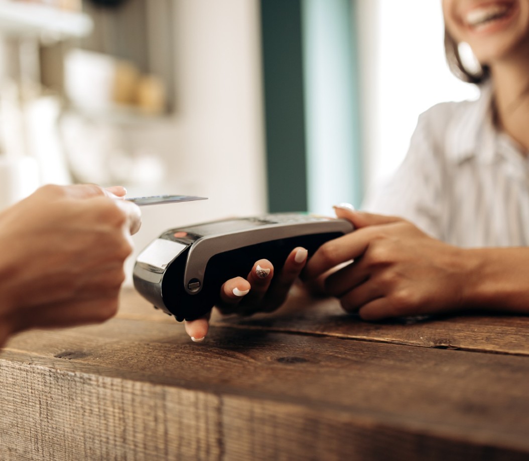 A customer tapping a card on a countertop payment terminal held by a shop owner